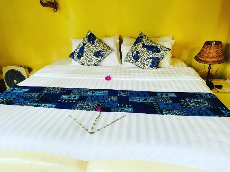 A king-size bed with blue and white kitenge cushions in the Family Cottage.