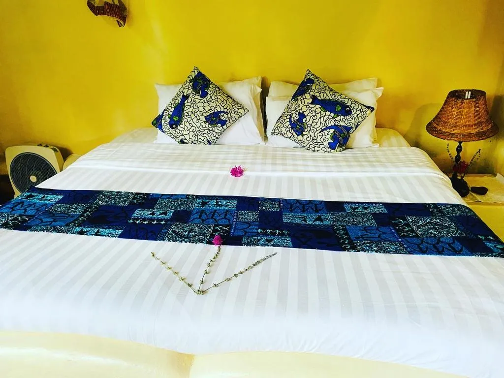 A king-size bed with blue and white kitenge cushions in the Family Cottage.