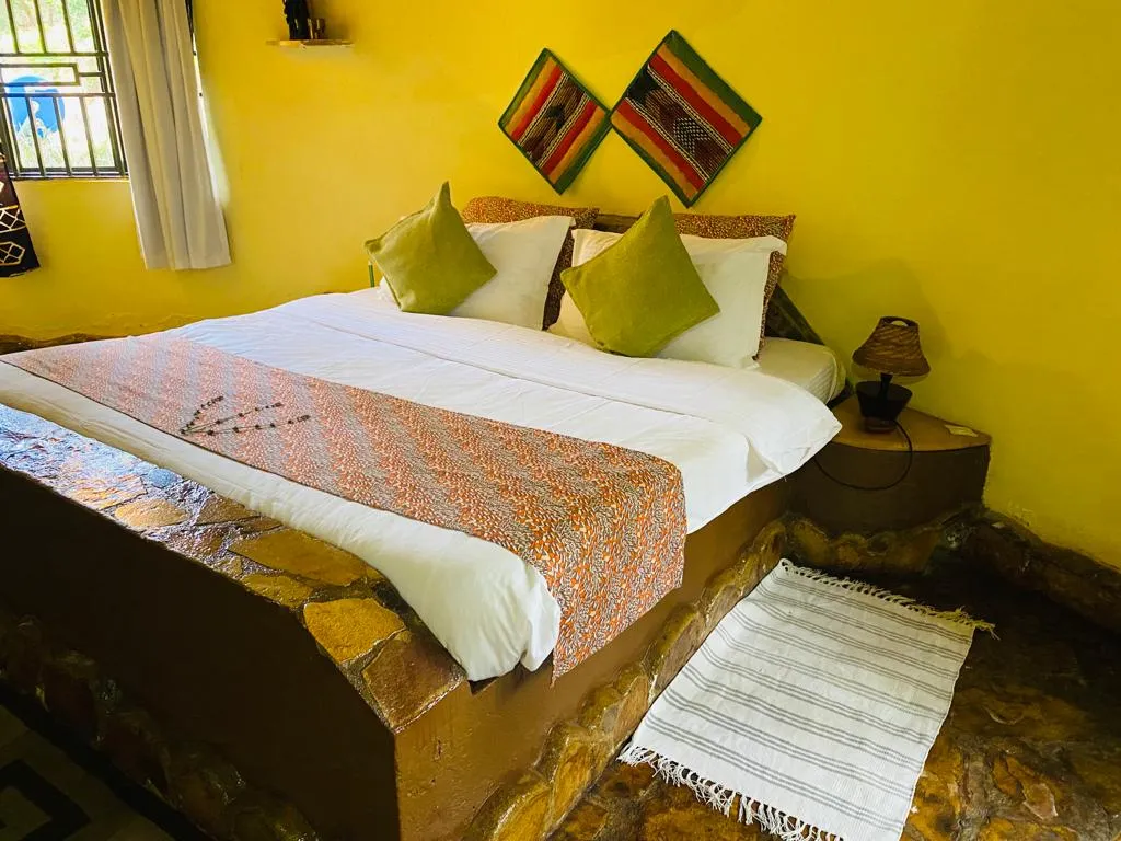 The Mango Cottage bedroom with a king-size bed, kitenge cushions and stone floor.