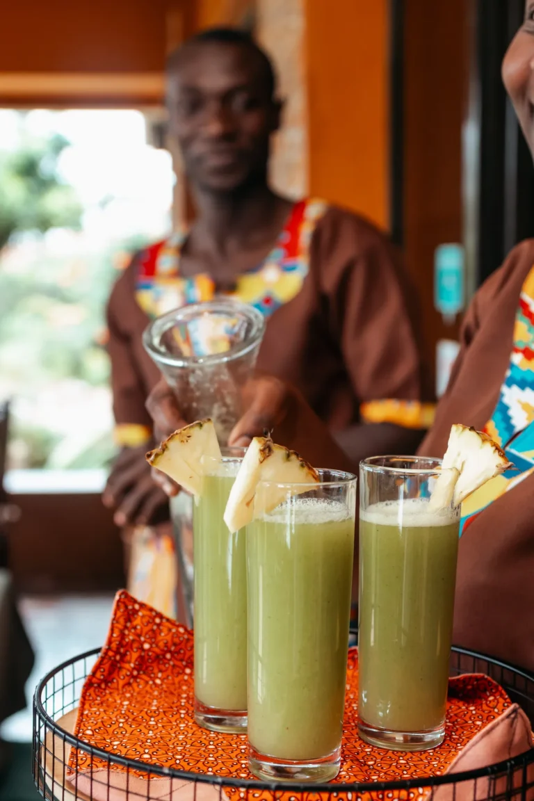 A Nyore host in a patterned shirt carries a tray of fresh welcome juices.