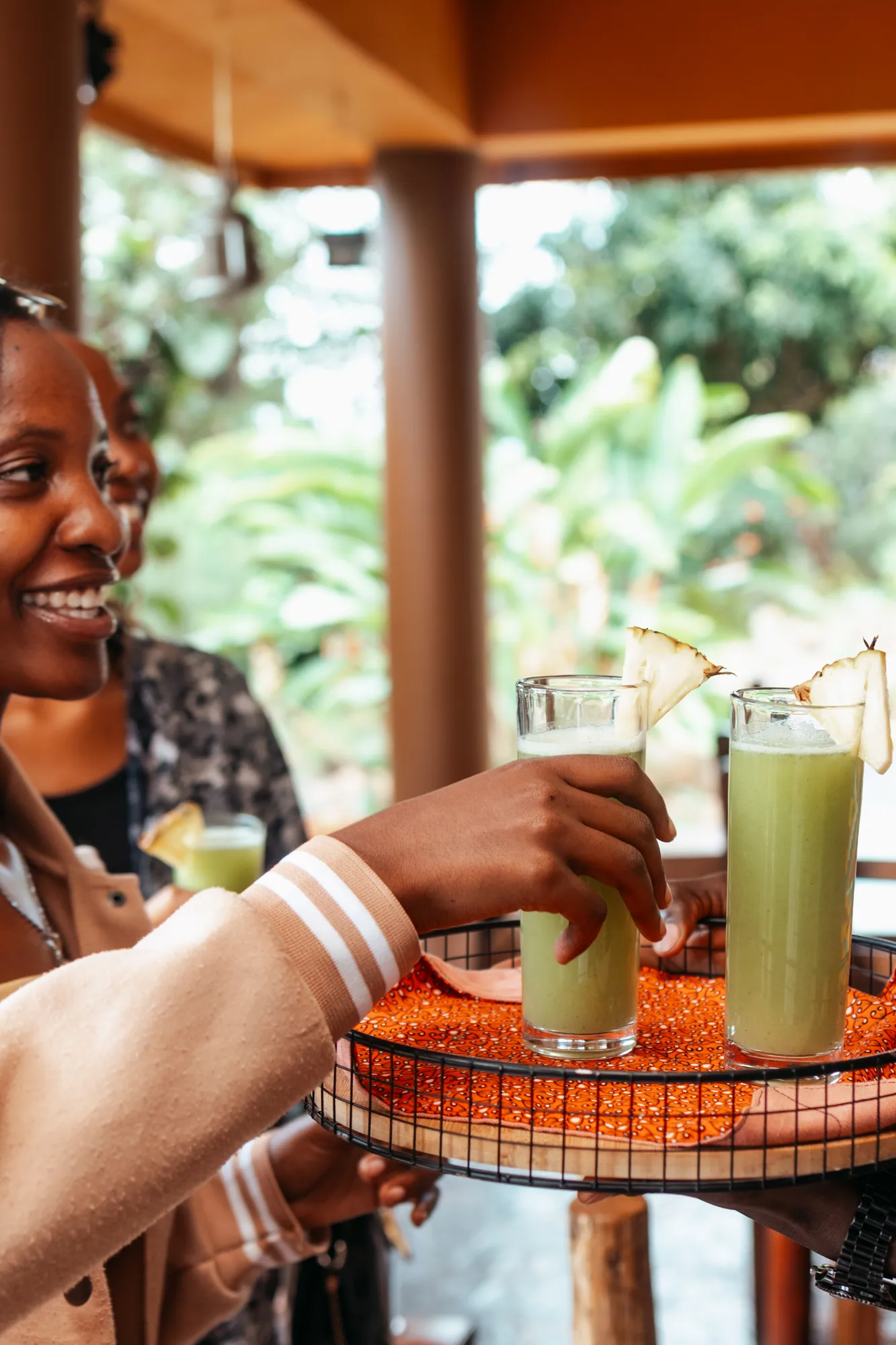 A smiling guest takes a welcome juice from a woven tray on the veranda.