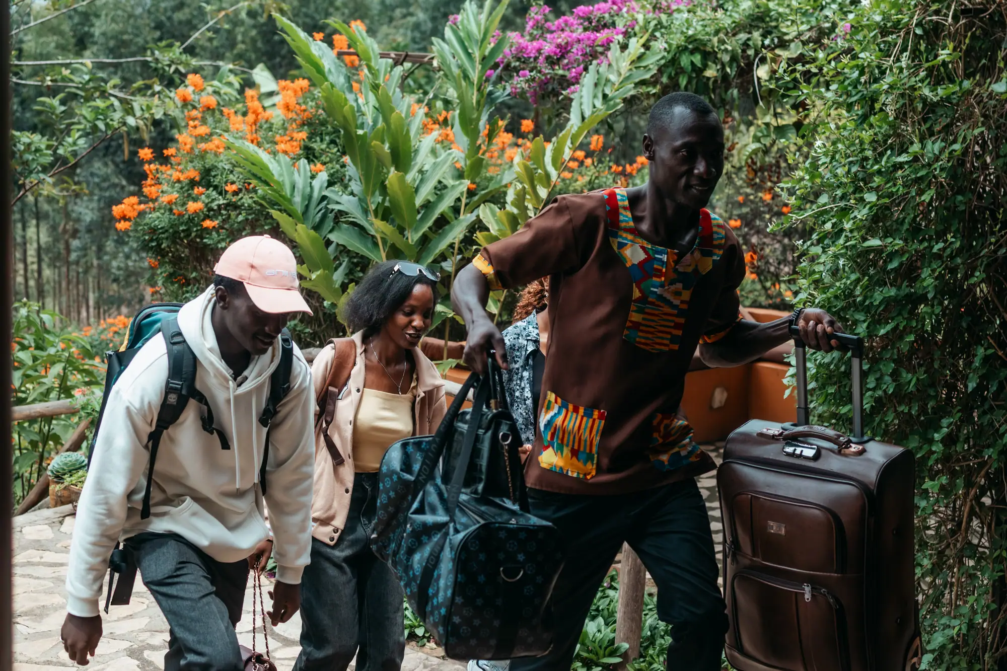 A Nyore host helps arriving guests with their luggage through the flowering garden.