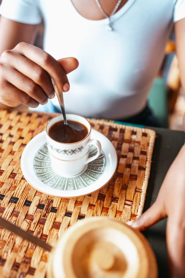 A guest stirs a cup of coffee at a table with woven placemats.