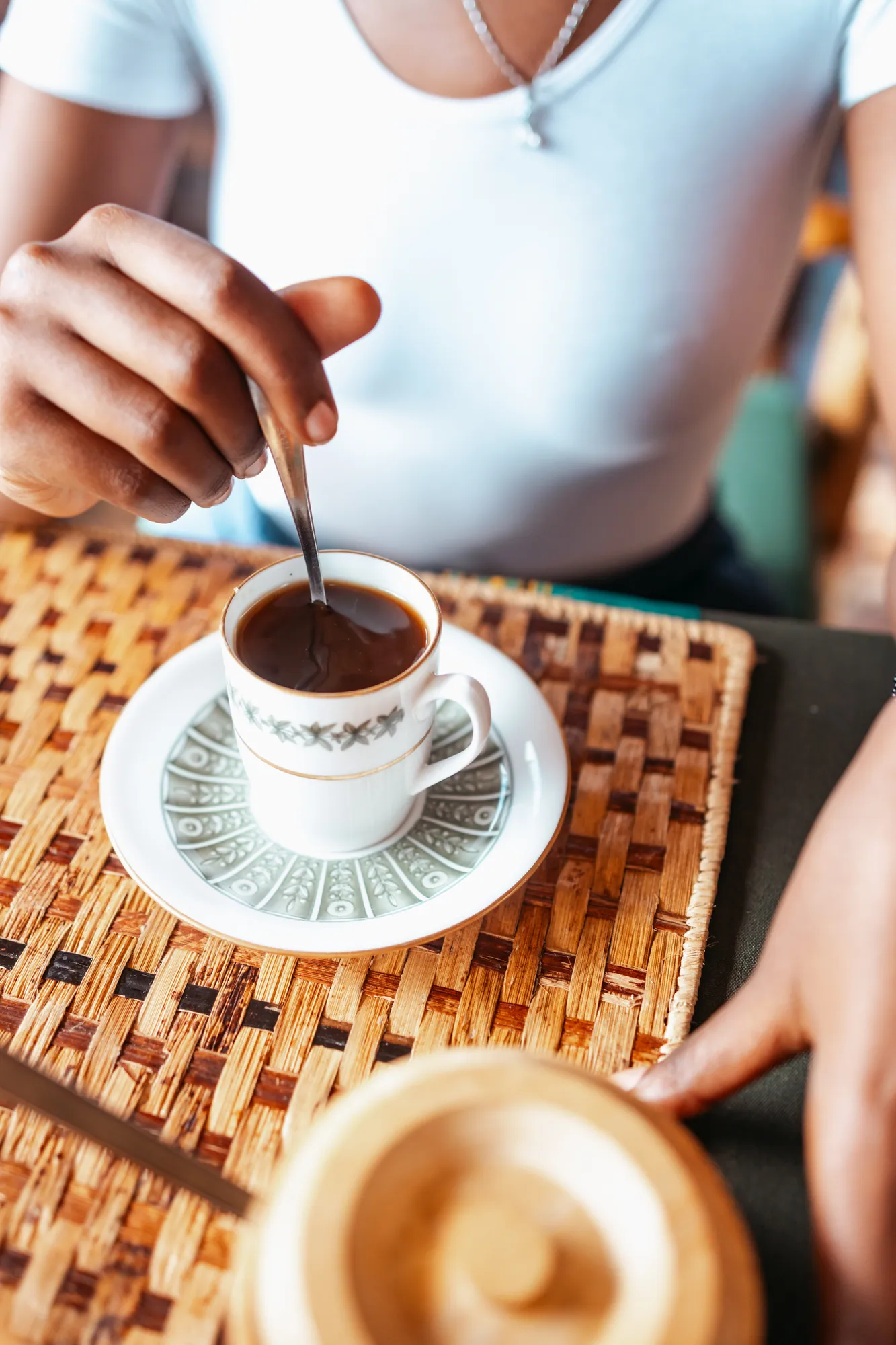 A guest stirs a cup of coffee at a table with woven placemats.
