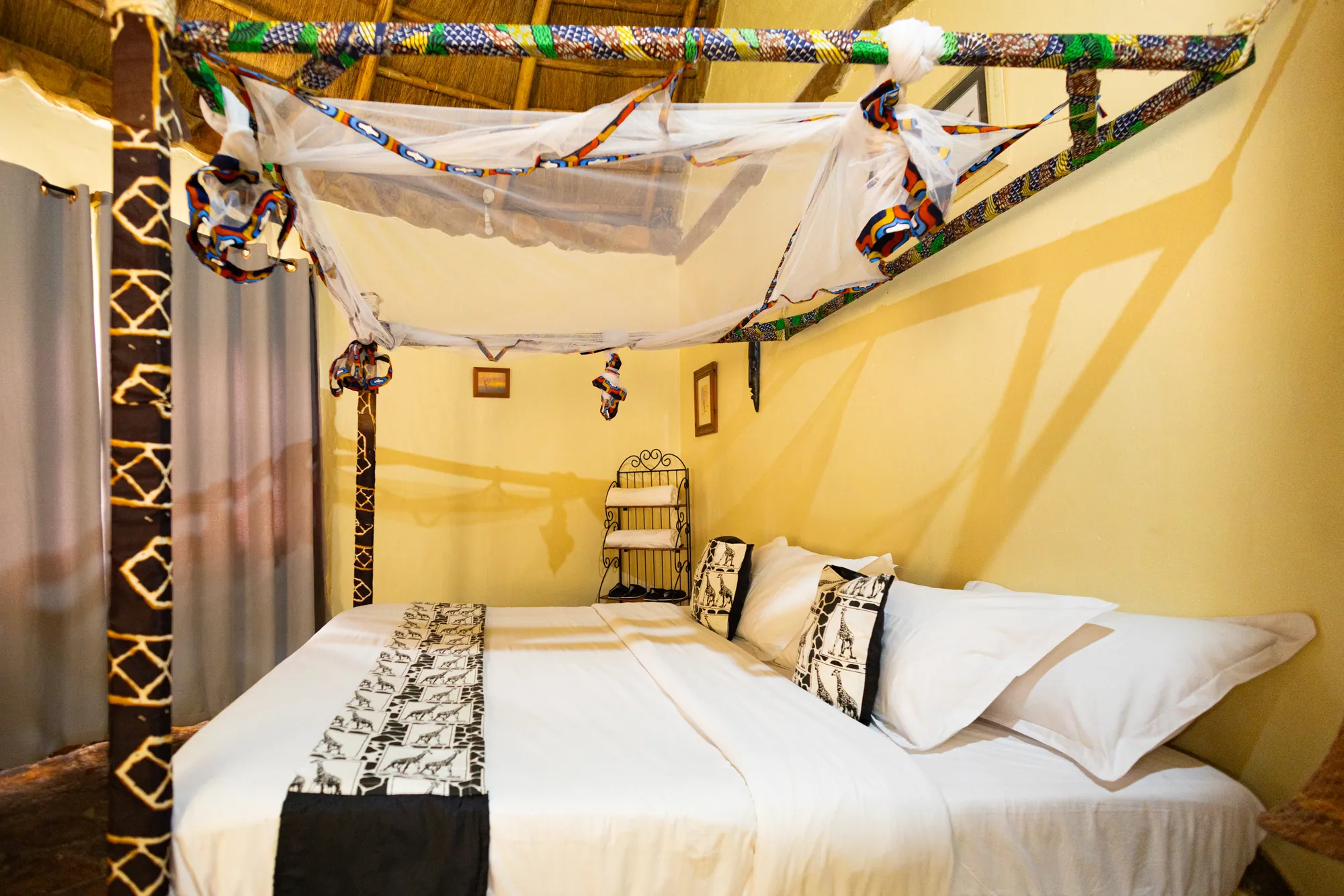A cottage bedroom with a canopy bed, mosquito net and printed bed runner.