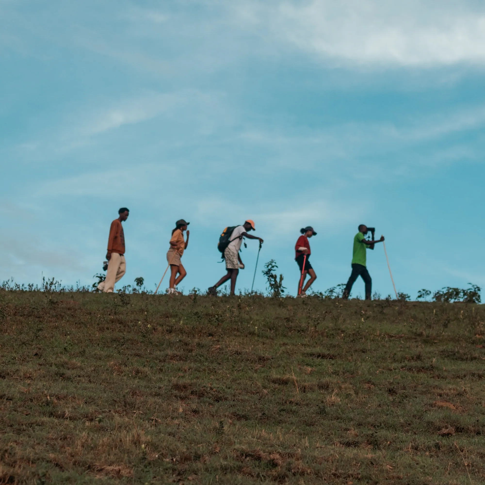 A group walks with hiking poles along a grassy ridge beneath an open sky.