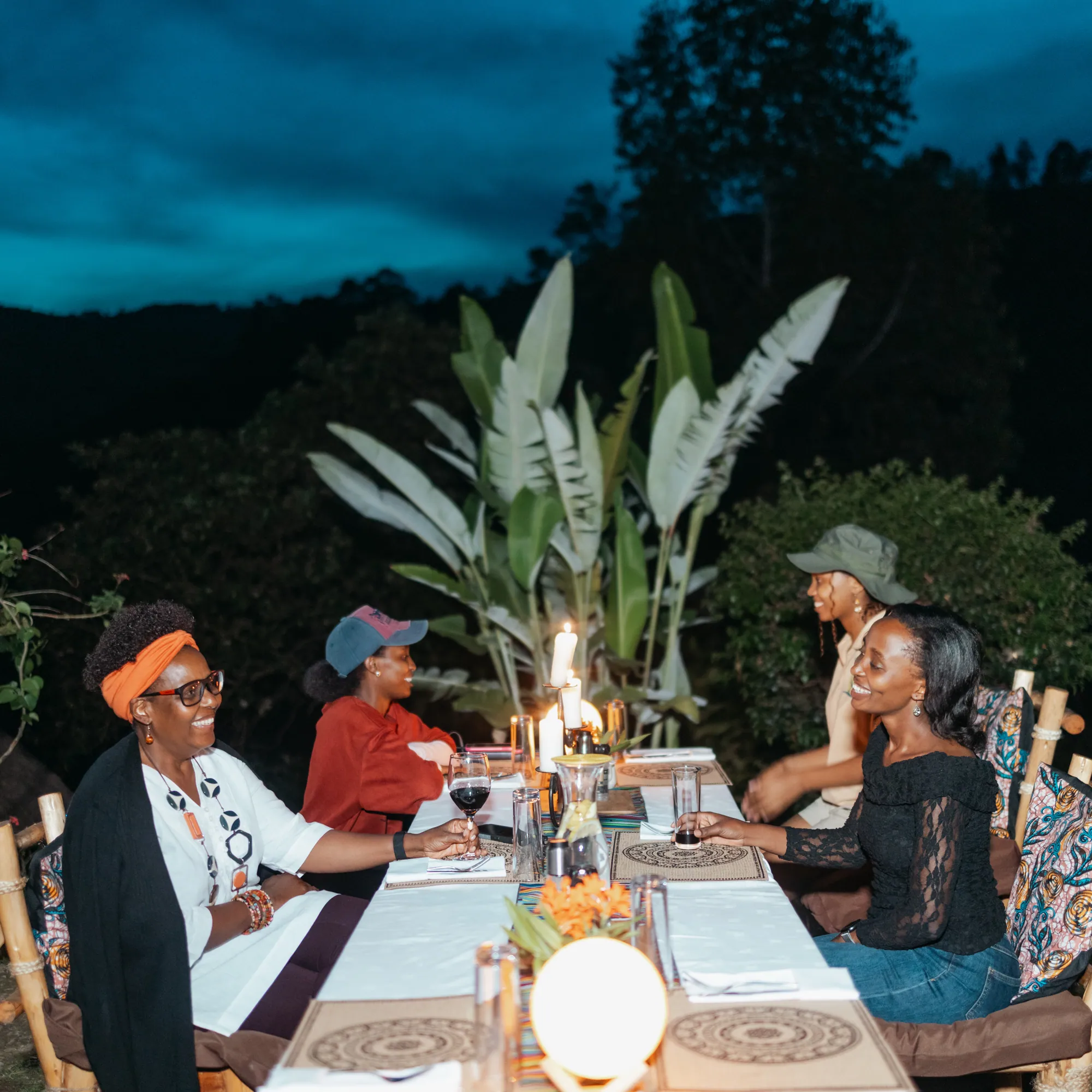 Guests share a candlelit dinner outdoors at dusk.