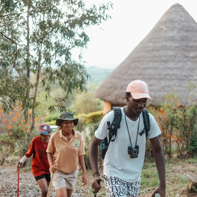 Hikers walk up the path past a thatched hut.